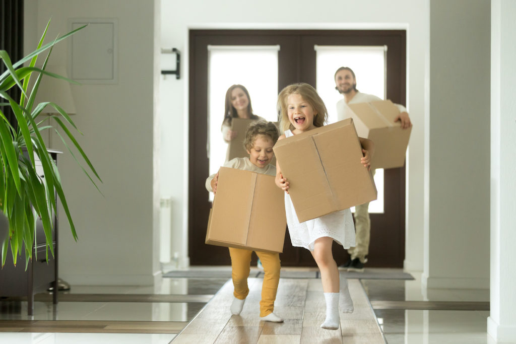 Happy family with parents and two kids carrying moving boxes into a new home